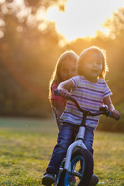Cute little boy riding a bike while his sister helping him in public park