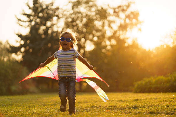 Full length of cute boy pretends to fly while playing with a kite in the public park