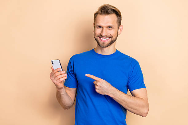 istock Photo of young man indicate finger mobile app download button recommend select isolated over beige color background 2212377821