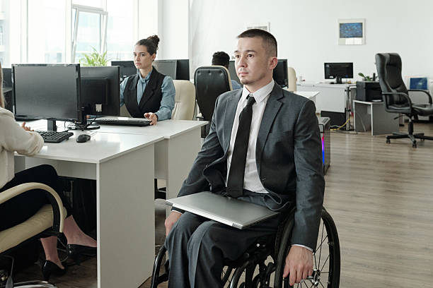istock Disabled businessman with laptop moving along open space office 2212378377