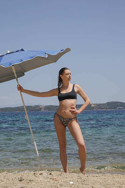 istock Woman enjoying hot summer day on the empty sand beach with blue sun umbrella 2212378900