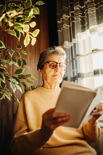 istock Senior caucasian woman reading book by the window 2212379411