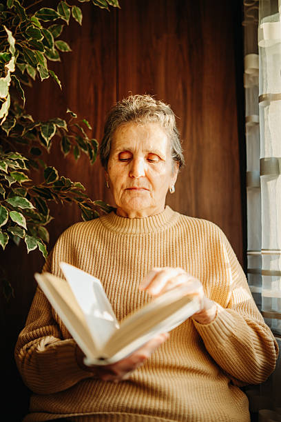 istock Senior caucasian woman reading book by the window 2212379420