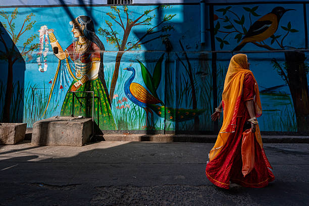 India. State of Rajasthan. Jodhpur. An Indian woman in a red sari walks past a mural on a city street