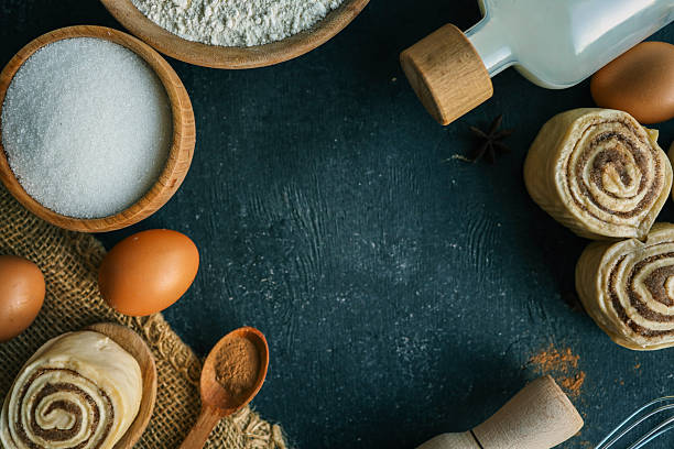 istock A top-down view of cinnamon buns on a dark surface with flour, sugar, eggs, milk, and a rolling pin, perfect for baking and recipe themes. 2212394688