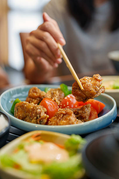Hand Holding Fried Chicken with Japanese Set Meal on Table