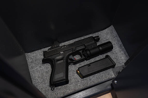 istock Modern black pistol with tactical light and red dot sight, securely stored in a safe with a magazine for self-defense. 2212397829