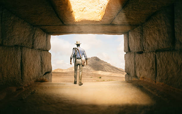 An adventurous explorer makes his way down a stone corridor to find it opens up, revealing a vast desert scene ahead. Scale model photography.