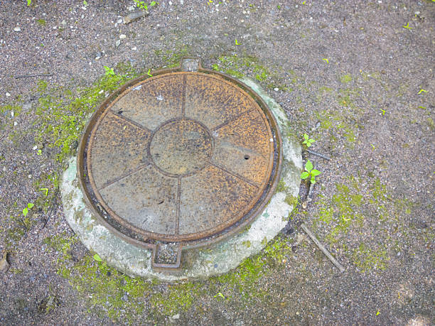 istock Rusty Manhole Cover with Moss and Small Stones on Weathered Concrete Base 2212399898
