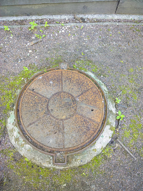 istock Rusty Manhole Cover with Moss and Small Stones on Weathered Concrete Base 2212400281