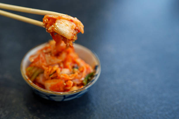 Close-up of a woman hand picking up fresh Korean kimchi from a patterned bowl using chopsticks, highlighting traditional Korean cuisine.