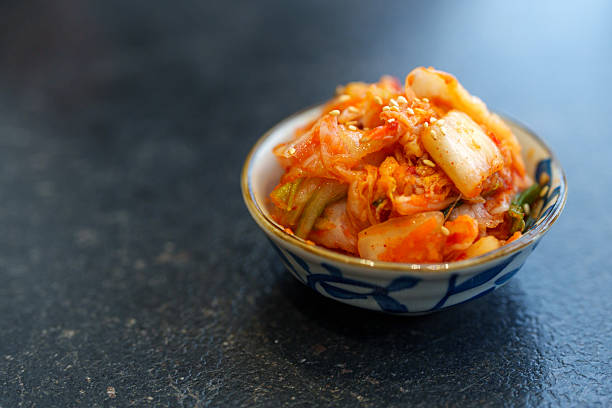 A close-up of freshly made Korean kimchi served in a small decorative bowl, placed on a dark textured table surface.