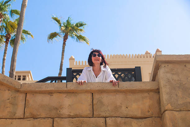 A woman bends over and looks down from a balcony.