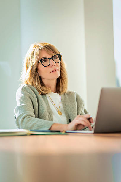 istock Blond haired businesswoman sitting in a modern office and using her laptop 2212414322