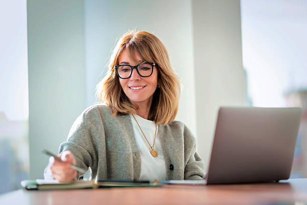 istock Blond haired businesswoman sitting in a modern office and using her laptop 2212414325