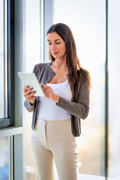 istock Attractive brunette haired businesswoman standing in a modern office and using her digital tablet for work 2212414659