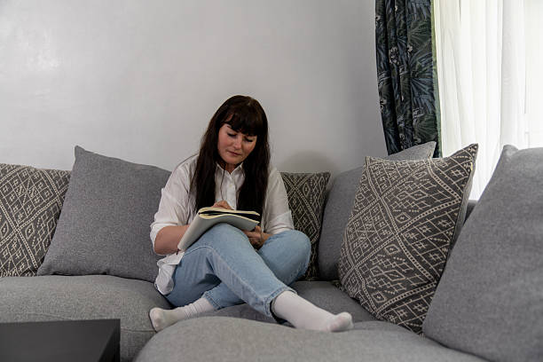 istock Woman writing on notebook sitting on comfortable sofa at home 2212417509