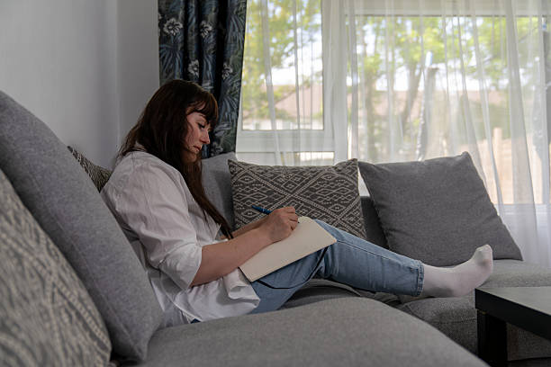 istock Woman writing on notebook sitting on sofa in living room 2212417512