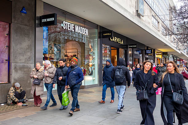 Contrasting lifestyles. Shoppers walking along Oxford Street in the West End of London while an unfortunate homeless man sits on the pavement, hoping for financial assistance.