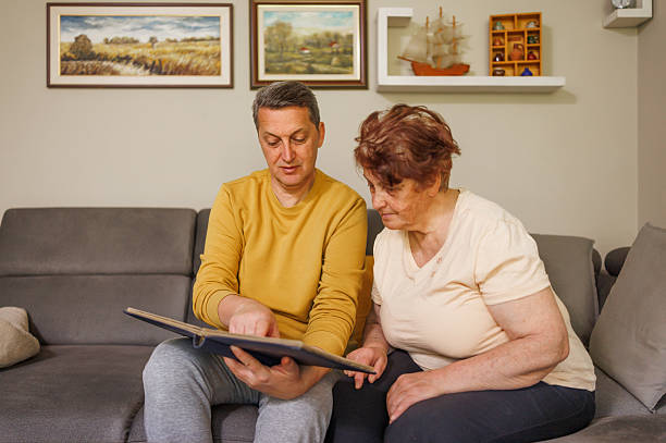 Adult son spending quality time with his aging mother, looking at a photo album full of old family memories