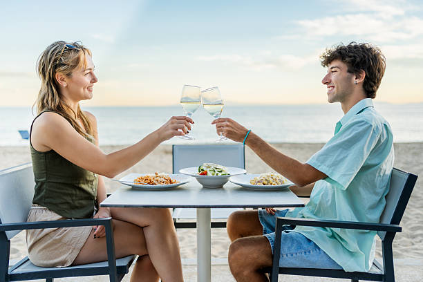 istock Young couple toasting with white wine at beach restaurant enjoying romantic dinner 2212426603