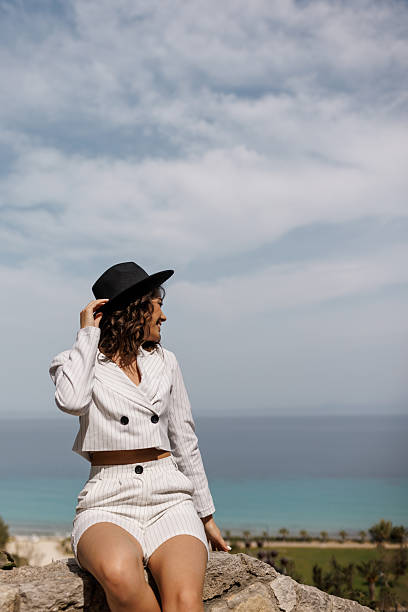 Portrait of beautiful young woman sitting on stone wall and relaxing in old coastal town