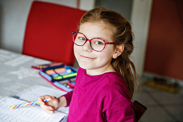 istock Little school girl learning at home. Elementary class student chid doing maths homework, writing with pencil. Happy pupil with eye glasses 2212430538