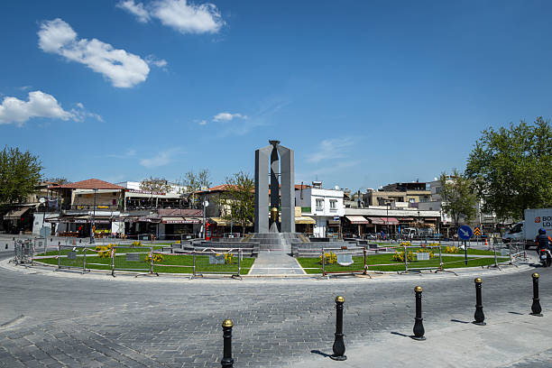 Gaziantep, Turkey - April 18, 2025: This image captures a roundabout in Gaziantep, Turkey, featuring a contemporary monument at its center. The surrounding area includes shops, low buildings, and a clear blue sky with scattered clouds.