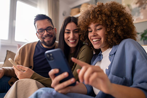 istock Three Happy Friends Relaxing on Couch Smiling and Sharing Moments While Using Smartphones 2212432767