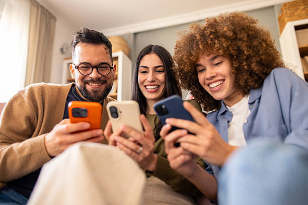 istock Smiling Diverse Friends Relaxing on Couch Sharing Laughter While Engaging with Smartphones 2212432780