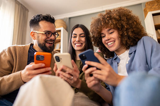 istock Diverse Young Friends Laughing Together While Checking Their Smartphones On Cozy Sofa 2212432894