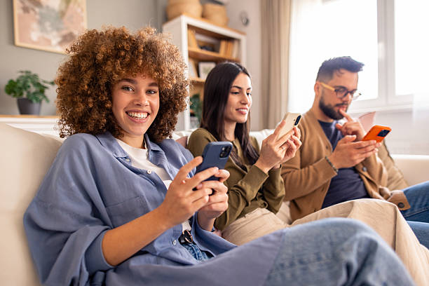 istock Three Friends Smiling and Chatting on a Cozy Couch While Using Smartphones 2212432895