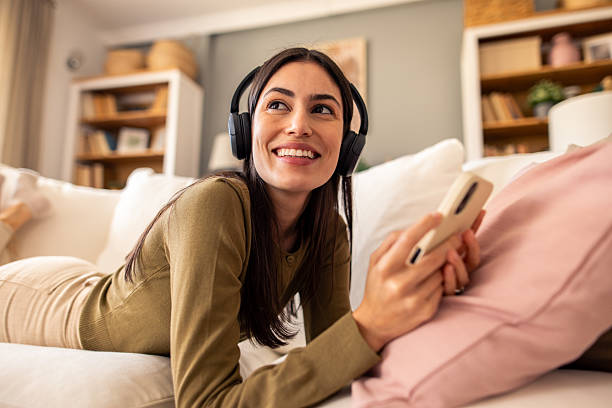 istock Young Woman With Wireless Headphones Smiling While Using Smartphone On Comfortable White Couch 2212432924
