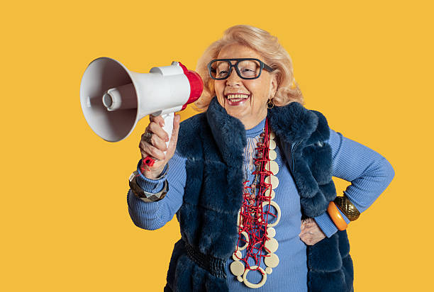istock Senior woman speaking into megaphone on yellow background 2212433851