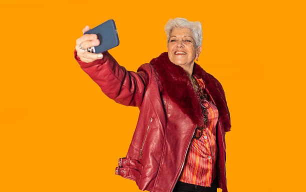 istock Senior influencer taking a selfie with smartphone on orange background 2212434800