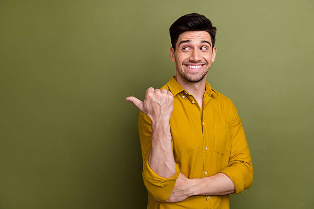 istock Portrait of nice positive man beaming smile look indicate thumb finger empty space isolated on khaki color background 2212436416