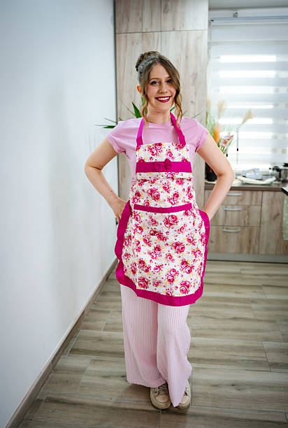 Young woman wearing pink apron, smiling and standing in a domestic kitchen