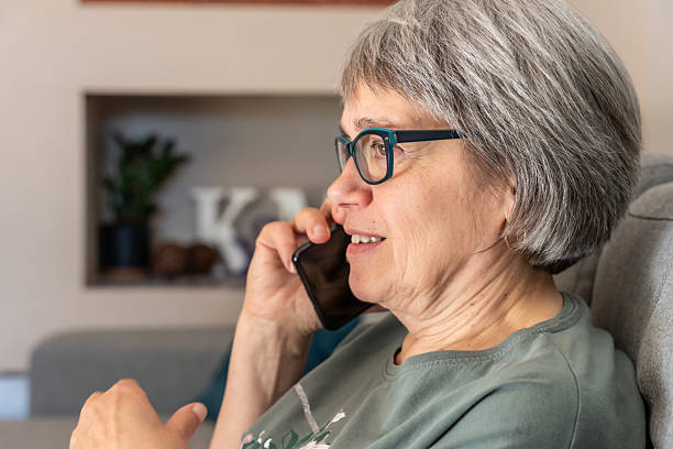 istock Elderly woman talking on smartphone while sitting on sofa in cozy home interior, focused on conversation, concept of communication and connection 2212440193