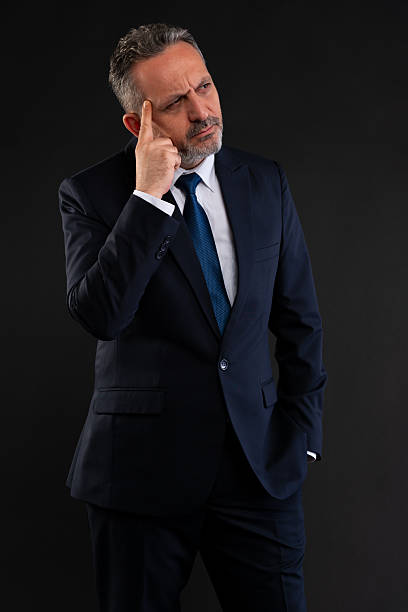 Mature businessman in suit pointing to his head, symbolizing critical thinking, planning, or intelligence.