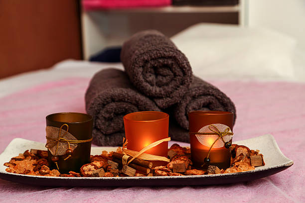 Balanced dark spa stones arranged in a stack with soft rolled towels and pastel flowers in the background. Warm beige setting creates a calm and serene mood. Perfect for wellness, spa, or meditation concepts.