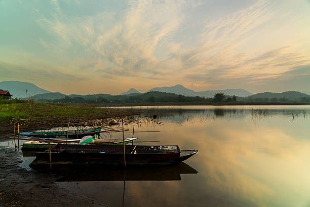 Vibrant sunset colors reflecting on the surface of a calm lake, with silhouettes of mountains in the background and a cloudy sky completing the serene landscape