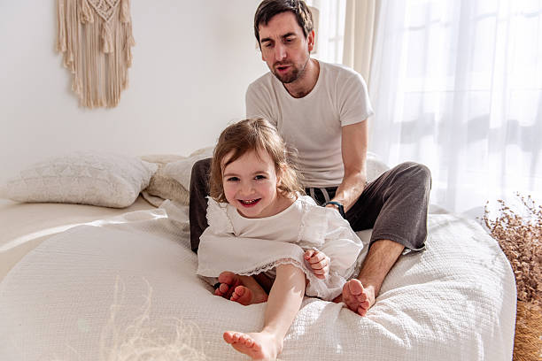 istock Happy daughter smiling and playing on bed with father 2212446098