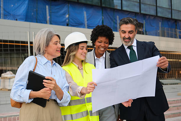 istock Architects and engineers discussing blueprint in front of building under construction 2212451480