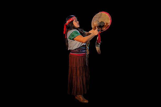 Young adult woman playing a traditional pre-hispanic dance with drum and mallet on black background
