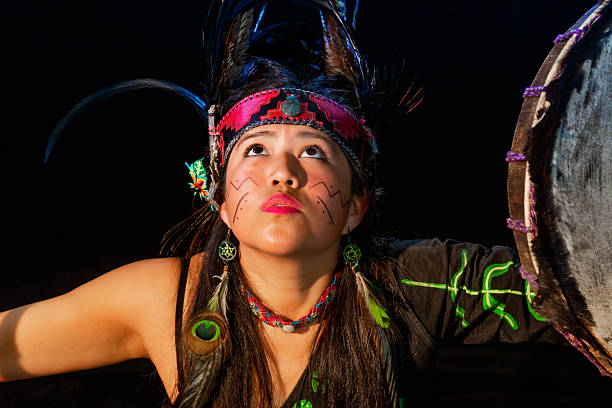 Young woman with colorful pre-hispanic inspired makeup and headdress playing a traditional drum
