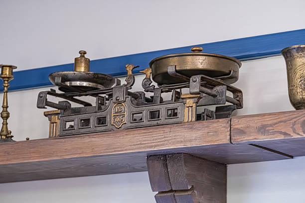Shelf with antique brass containers and mechanical equipment against a light wall with dark stripe Objects include scales, weights, testing devices Arranged casually, no order Warm, ambient lighti