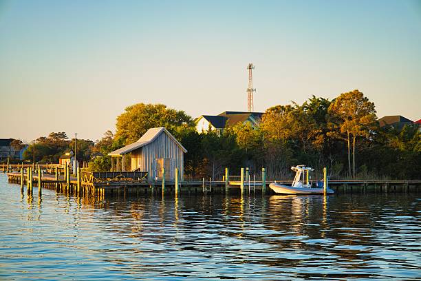 A nice bay view at sunrise of a wooden shack on the corner of a wooden dock and a motorboat at Roanoke Marshes area on Roanoke Island in Manteo, North Carolina USA.