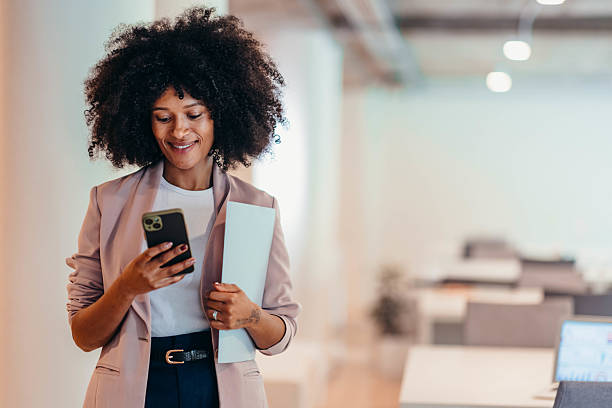 istock Smiling businesswoman using smartphone and holding documents in office 2212460058