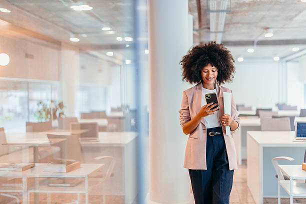 istock Smiling businesswoman using smartphone and holding documents in modern office 2212460593