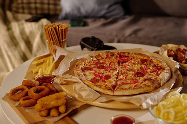 Pepperoni and cheese pizza with various snacks, including onion rings, on white table in cozy indoor environment with sofa in background